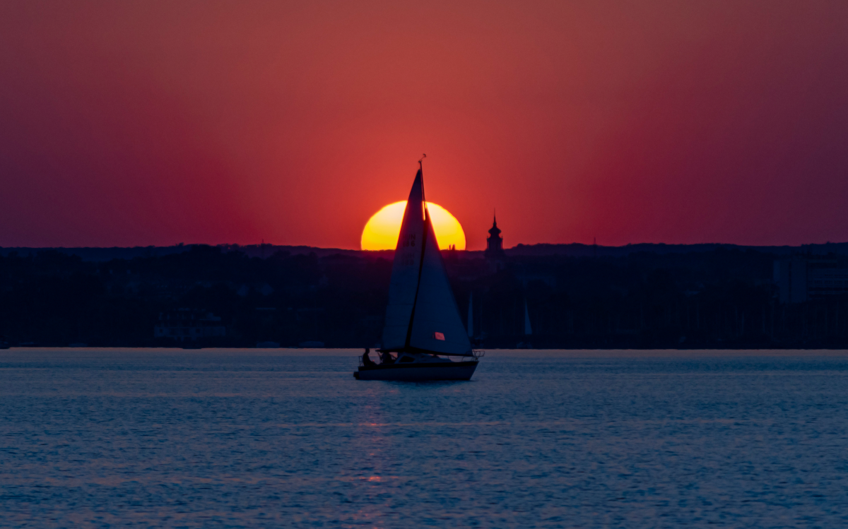 Sunset on Lake Balaton with a sailboat, with the tower of the Festetics Castle in the background